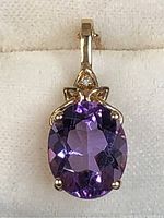 Close-up of oval amethyst pendant with diamond accent and gold bail on fabric background