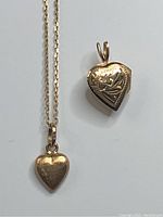 Gold chain with small smooth heart pendant alongside larger etched heart locket pendant