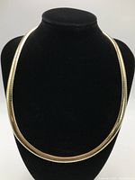 Front view of polished gold Omega style necklace displayed on black bust