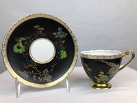 Front view of Shelley Exotic Bird black cup and saucer set, showing gold gilded trims, enamel floral and bird decorations on black background.