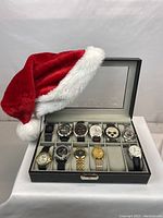 Assorted wristwatches in leather and metal straps displayed in a black storage case with a Santa hat