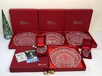 Four Waterford Crystal Christmas plates displayed in red original boxes with three boxes open and one closed, two small crystal Christmas ornaments boxed in red velvet cases, with accompanying papers and small decorative balls.