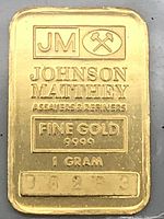 Close-up front of bar showing JM logo, crossed hammers, JOHNSON MATTHEY ASSAYERS & REFINERS, FINE GOLD 9999, 1 GRAM, serial 98283