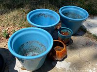 Three large blue glazed pots with two smaller pots, one blue glazed and one brown glazed, shown outside on pavement and grass. Showing dirt, use marks and some chips and cracks.