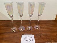 Four iridescent champagne flutes standing upright on a wooden surface with gold stickers on the bases, photographed against a plain white background.