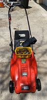 Front view of the Orange Black & Decker cordless electric lawnmower showing handlebars and branding.