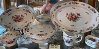 Photo showing entire set arranged on glass surface, multiple serving pieces including platters, tureen, creamer, and sugar bowl, all with floral pattern and gold trim.