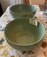 Two green ceramic nesting bowls shown side by side, highlighting embossed acorn pattern on rim and nesting size difference.