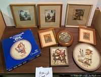 Full lot overview showing various framed prints, plaques, music box, and commemorative plates arranged on table.