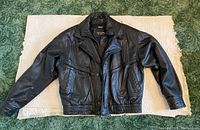 Full front view of a black leather jacket laid flat showing overall shape and design.