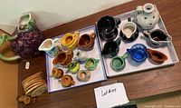 Overview of trays with miniature pitchers, grape-shaped pitcher, and coaster set on wooden surface.
