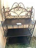 Front view of small black wrought iron folding bookshelf showing three shelves and decorative scrollwork on sides and back