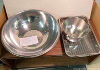 Two large stainless steel bowls, one with handles, placed adjacent to a stainless steel steam pan with removable tray inside.