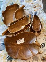 Photo showing all six vintage Monkey Pod wood bowls arranged on floral cloth, varying sizes and shapes visible including leaf and pod shapes with handle extensions.
