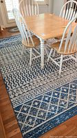 Surya area rug under dining table showing the pattern and coloring, mainly blue and white geometric designs, photo taken to display rug size and condition.