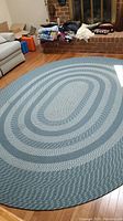 Oval braided area rug on hardwood floor, showing blue and white concentric braided pattern.