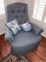 Front view of gray upholstered recliner armchair showing button tufted backrest and two pillows on seat.