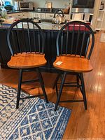 Pair of wooden bar stools with black spindle backs and natural wood contoured seats, positioned in a kitchen setting.