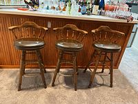 Front view of the three wooden bar stools with padded dark brown seats and spindle backrests.