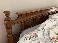 Close-up view of the top and side details of the wooden bed frame headboard showing the wood finish, baluster posts, and detailed paneling.