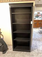 Front view of black wooden bookcase showing four shelves and surface scratches