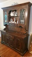 Front view of the entire two-piece wooden china cabinet with displayed figurines and decorative glass-paneled doors
