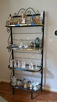 Full view of black metal and glass display shelf with various small figurines on shelves, placed against wall.