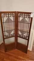 Full view of the two-panel wood divider screen with geometric cutout pattern and solid wood bottom panels.