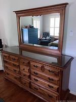 12 drawer wooden dresser with attached large wooden framed mirror and glass protective top, shown in a room with hardwood floor.