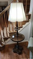 Front view of the vintage wooden lamp table with round tabletop and fabric lamp shade, showing decorative inlay on table surface.