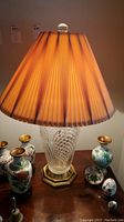 Photo of the glass base lamp with brown pleated shade lit, showing shade color and pleating details.