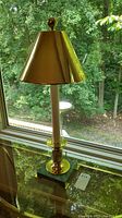 Full view of the lamp with stone base, brass column and gold metallic lampshade next to window