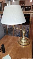 Brass table lamp with round base and white fabric shade on wooden table beside a flashlight