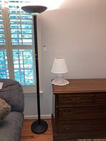 Full view of the black metal floor lamp and white ceramic table lamp on wooden dresser.