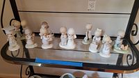 Ten Precious Moments figurines arranged on a glass shelf, displaying various scenes and poses.