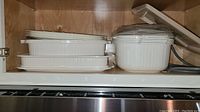 Three nested white rectangular casserole dishes and large vented microwave container stored on shelf