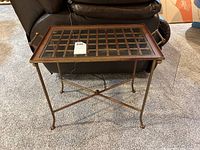 Front view of metal framed side table with beveled glass top tray placed on carpet in front of couch.