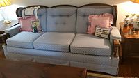 Full view of blue upholstered sofa with attached back cushions and three seat cushions, showing blue quilted fabric and decorative throw pillows with text and ruffles.