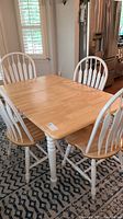 Full view of dining table and four chairs from a corner angle, showing natural wood table top and white painted legs and chair backs.