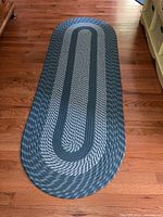 Photo showing one oval braided rug in blue and gray tones on hardwood floor.