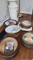 Several stacks of round decorative plates with colorful, detailed illustrations including children, animals, and thematic scenes. Some are framed in brown wood.