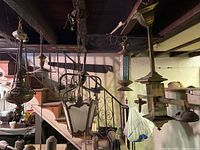 Photo showing six antique hanging light fixtures including three gas chandeliers and three electric fixtures with metal chains, decorative elements, and varying conditions.