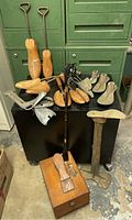 Full view of antique cobbler tools including wooden and metal shoe stretchers, shoeshine box, and horse shoe horn on black surface in basement