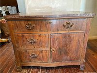 Front view of antique wooden wash cabinet with ornate drawers and marble top visible.