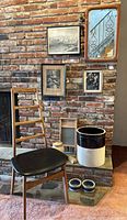 Full view of corner setup showing mirror, framed artworks, chair, washboard, ceramic crock, cookie jar, and bowls in front of brick wall.
