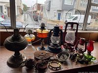 Six antique oil lamps of various styles and colors on a wooden surface including chimney glasses and assorted metal parts.