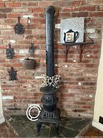 Front view of antique potbelly stove with butterfly iron decoration and wall-mounted vintage cast iron trivets and pot.