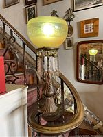 Antique gas light newel post positioned on a stair banister showing yellow etched glass globe and metal base with hanging crystals.