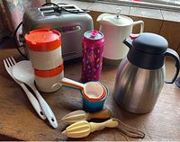 Photo showing all items from above: KitchenAid toaster, two thermoses, colorful nested measuring cups, wooden citrus reamers, large white plastic ladle and fork