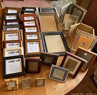 Collection of 26 assorted picture frames arranged on a wooden table, showing varied sizes and styles including both vintage and modern looks.